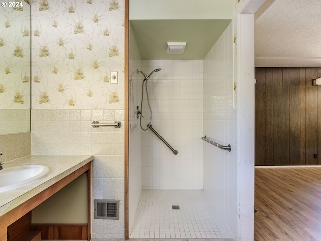 bathroom with a tile shower, vanity, and tile walls