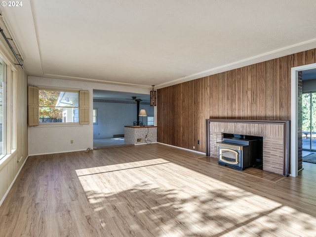 unfurnished living room featuring wood walls, crown molding, wood-type flooring, a wood stove, and a baseboard heating unit