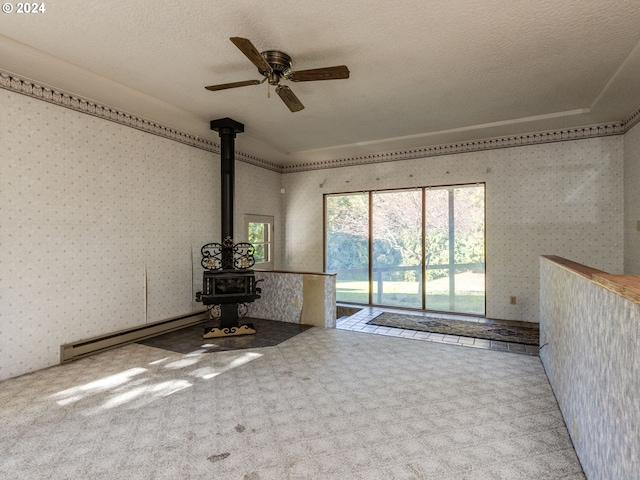 unfurnished room featuring ceiling fan, a baseboard heating unit, carpet flooring, a textured ceiling, and a wood stove