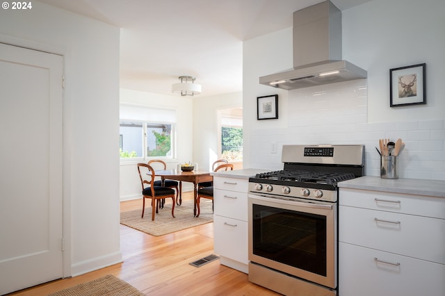 kitchen with tasteful backsplash, light hardwood / wood-style flooring, gas range, white cabinets, and exhaust hood