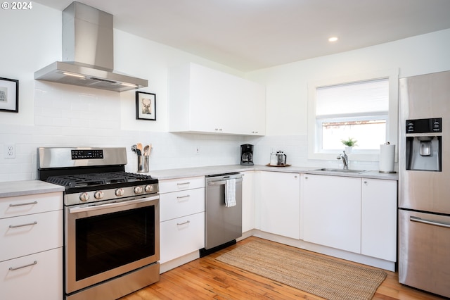 kitchen featuring sink, light hardwood / wood-style flooring, wall chimney range hood, white cabinetry, and stainless steel appliances