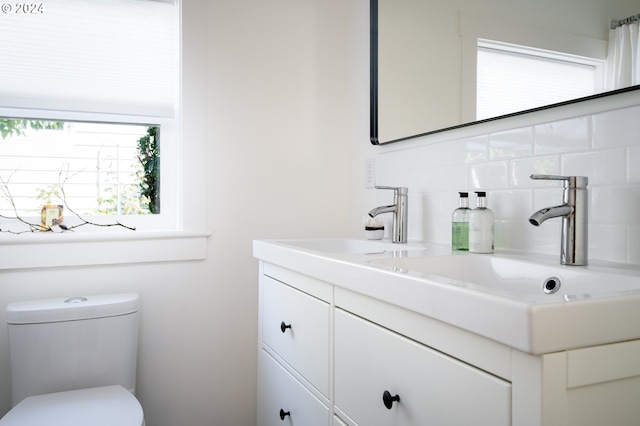 bathroom featuring backsplash, toilet, vanity, and a healthy amount of sunlight