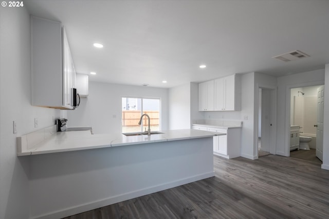 kitchen with kitchen peninsula, stove, sink, white cabinets, and dark hardwood / wood-style floors