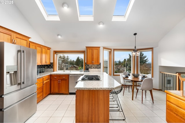 kitchen with light tile patterned flooring, appliances with stainless steel finishes, decorative light fixtures, sink, and light stone countertops