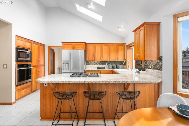 kitchen featuring appliances with stainless steel finishes, sink, a kitchen breakfast bar, kitchen peninsula, and light stone countertops