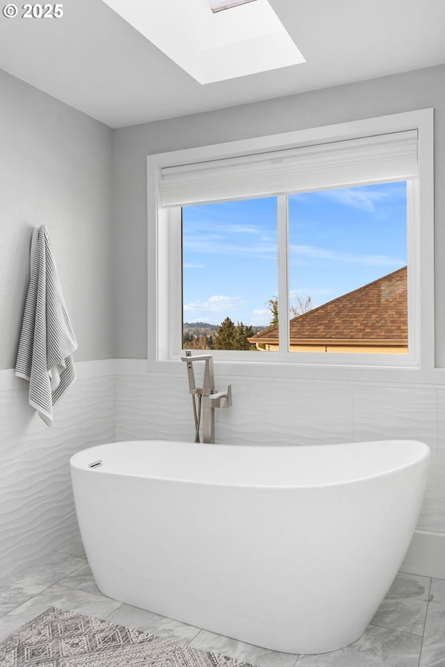 bathroom with a skylight, a bathtub, and tile walls