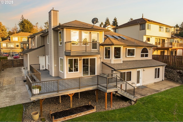 back house at dusk featuring a wooden deck and a patio