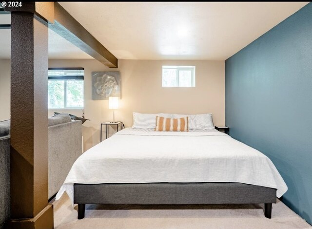 bedroom with multiple windows, light carpet, and beamed ceiling