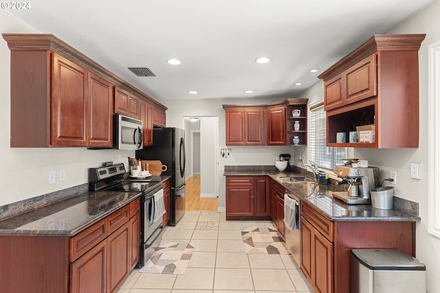 kitchen with appliances with stainless steel finishes, light tile patterned floors, dark stone counters, and sink