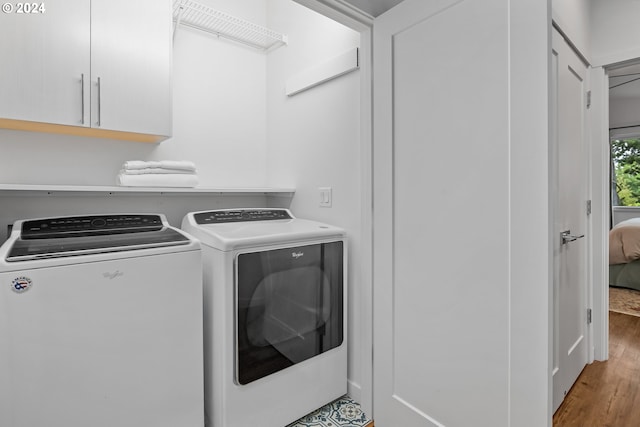 clothes washing area with light hardwood / wood-style flooring, washer and dryer, and cabinets