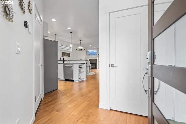 interior space featuring stainless steel appliances, sink, decorative light fixtures, light wood-type flooring, and white cabinetry