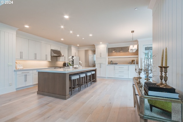 kitchen featuring a breakfast bar, a center island, pendant lighting, white cabinetry, and light hardwood / wood-style floors