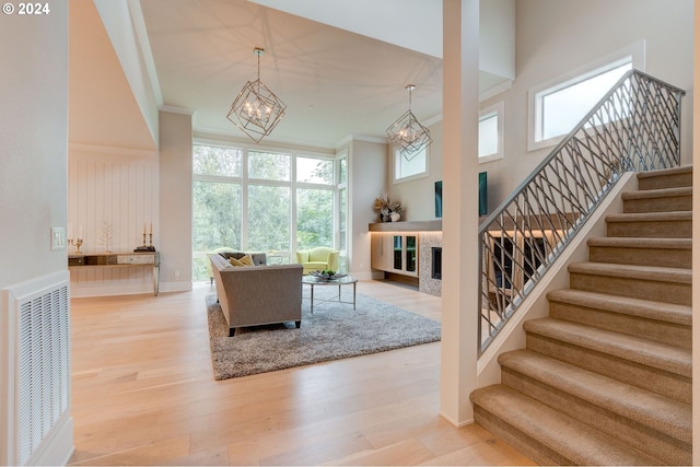 living room featuring a chandelier, light hardwood / wood-style flooring, crown molding, and a towering ceiling