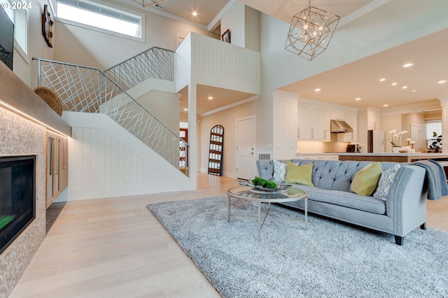 living room featuring a notable chandelier, light hardwood / wood-style flooring, crown molding, and a high ceiling