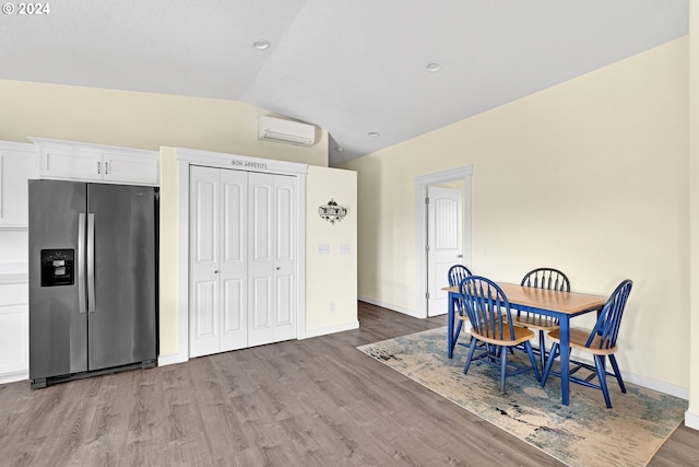 dining area with a wall mounted air conditioner, light hardwood / wood-style flooring, and vaulted ceiling