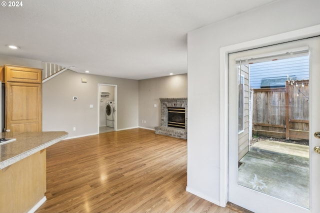 unfurnished living room with washing machine and clothes dryer, a brick fireplace, and light wood-type flooring