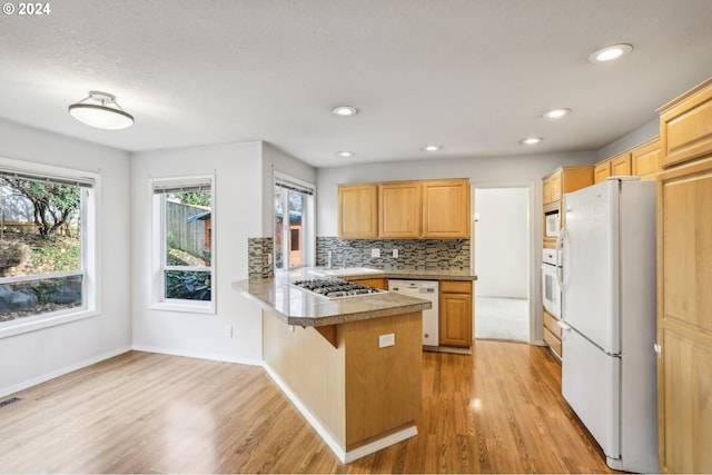 kitchen featuring kitchen peninsula, a kitchen bar, light brown cabinetry, white appliances, and light hardwood / wood-style floors