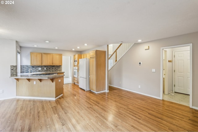 kitchen featuring a kitchen breakfast bar, white appliances, kitchen peninsula, and light hardwood / wood-style flooring