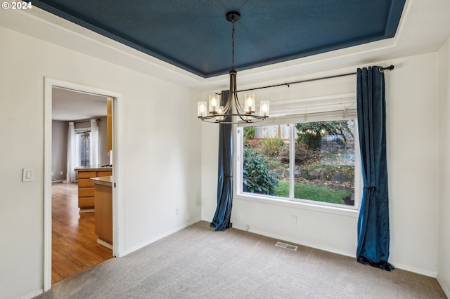 spare room with a raised ceiling, carpet floors, and a chandelier