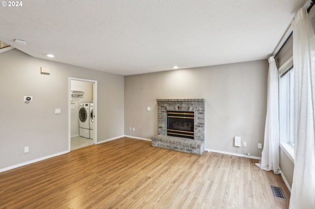 unfurnished living room featuring independent washer and dryer, light wood-type flooring, a brick fireplace, and plenty of natural light