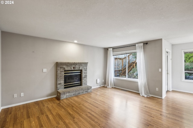 unfurnished living room featuring a textured ceiling, light wood-type flooring, and a brick fireplace