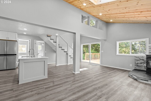 living room with a wood stove, light hardwood / wood-style flooring, sink, wooden ceiling, and high vaulted ceiling