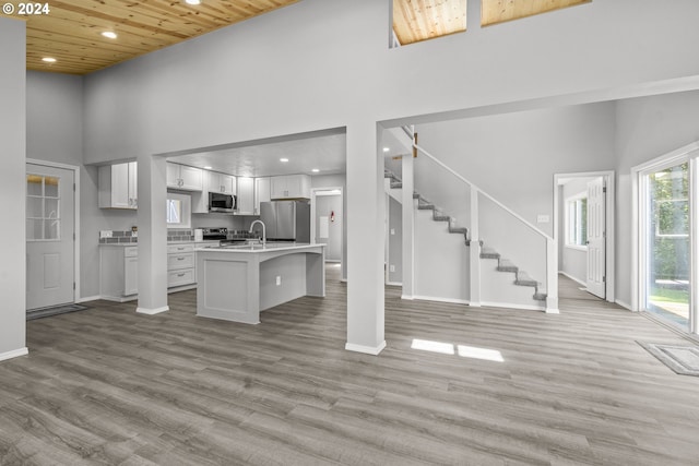 kitchen featuring appliances with stainless steel finishes, light hardwood / wood-style flooring, a towering ceiling, and white cabinets