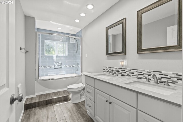 full bathroom featuring hardwood / wood-style floors, backsplash, vanity, toilet, and shower / bath combination with glass door