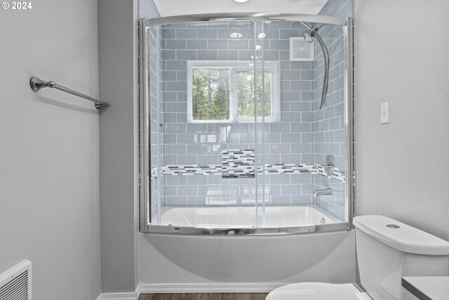 bathroom featuring toilet and combined bath / shower with glass door