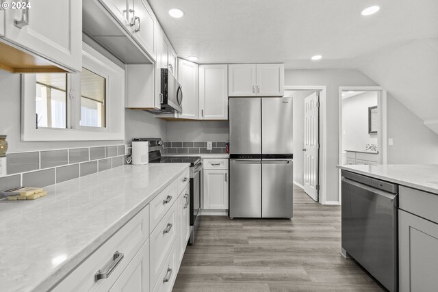 kitchen featuring light hardwood / wood-style flooring, stainless steel appliances, light stone countertops, white cabinets, and lofted ceiling