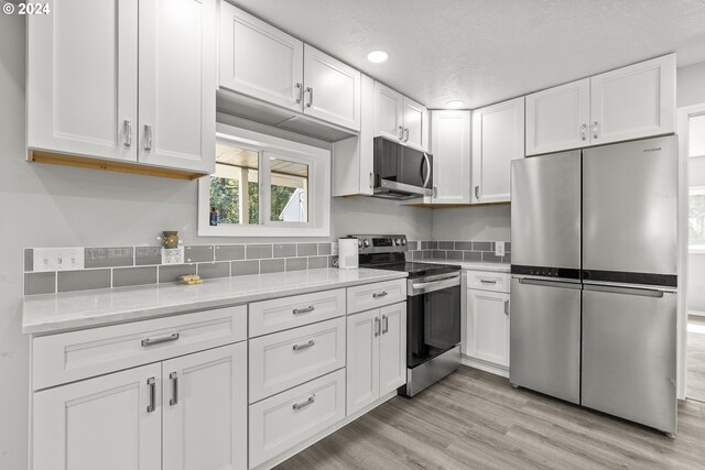 kitchen with light hardwood / wood-style floors, stainless steel appliances, white cabinetry, and light stone countertops