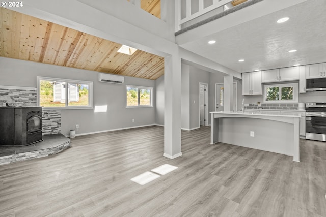 living room featuring an AC wall unit, a wood stove, wood ceiling, and light wood-type flooring