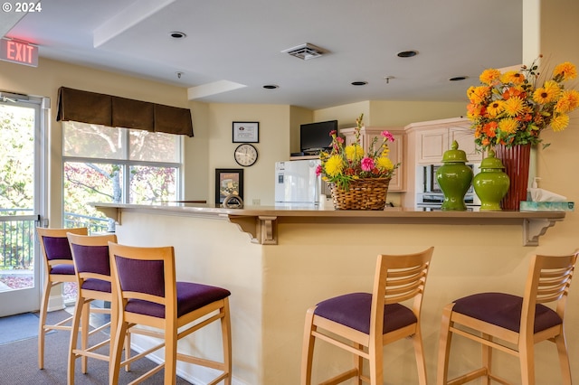 kitchen with white fridge, kitchen peninsula, light carpet, and a breakfast bar area