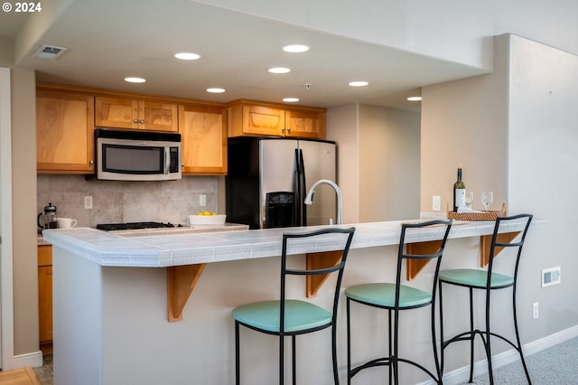 kitchen featuring kitchen peninsula, a kitchen breakfast bar, decorative backsplash, stainless steel appliances, and tile counters