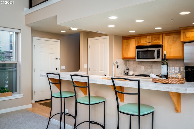 kitchen featuring kitchen peninsula, a kitchen breakfast bar, tasteful backsplash, sink, and light hardwood / wood-style flooring