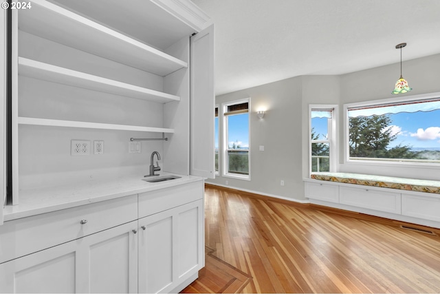 bar featuring light wood-style flooring, a sink, visible vents, baseboards, and pendant lighting