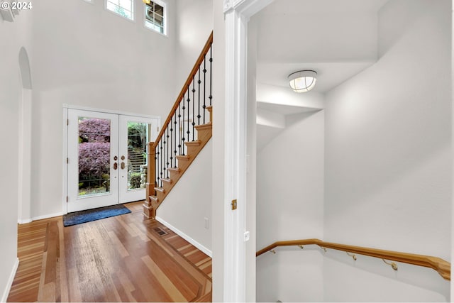 foyer featuring baseboards, wood finished floors, a high ceiling, stairs, and french doors