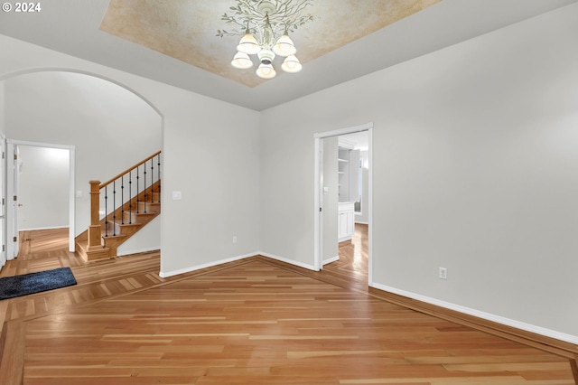 empty room featuring arched walkways, baseboards, light wood finished floors, and stairs