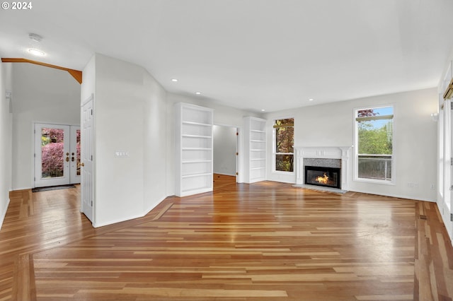 unfurnished living room featuring light wood-style flooring, recessed lighting, baseboards, built in features, and a glass covered fireplace