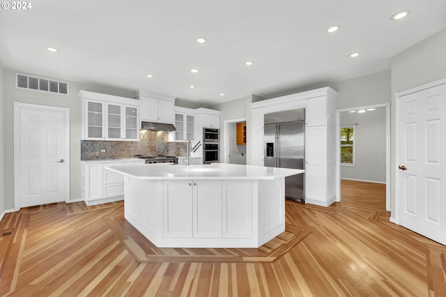 kitchen with visible vents, stainless steel built in fridge, light countertops, under cabinet range hood, and white cabinetry