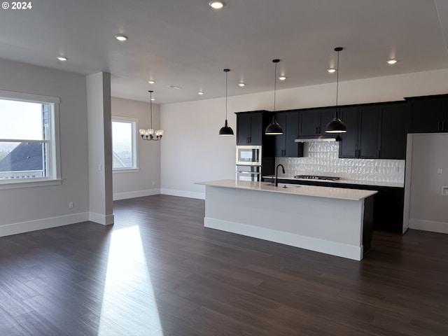 kitchen with dark hardwood / wood-style flooring, a center island with sink, pendant lighting, and appliances with stainless steel finishes