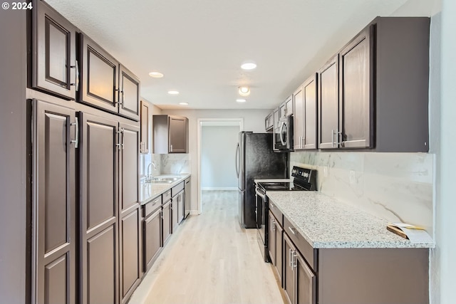 kitchen featuring light wood-type flooring, light stone counters, sink, decorative backsplash, and stainless steel appliances