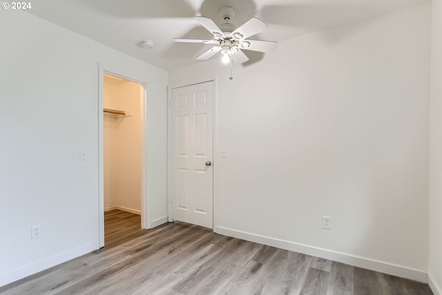 unfurnished bedroom with light wood-type flooring, ceiling fan, a walk in closet, and a closet