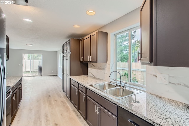 kitchen with light stone countertops, light wood-type flooring, dark brown cabinetry, and sink