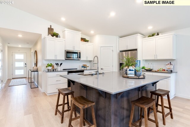 kitchen featuring a center island with sink, white cabinetry, stainless steel appliances, and a breakfast bar area