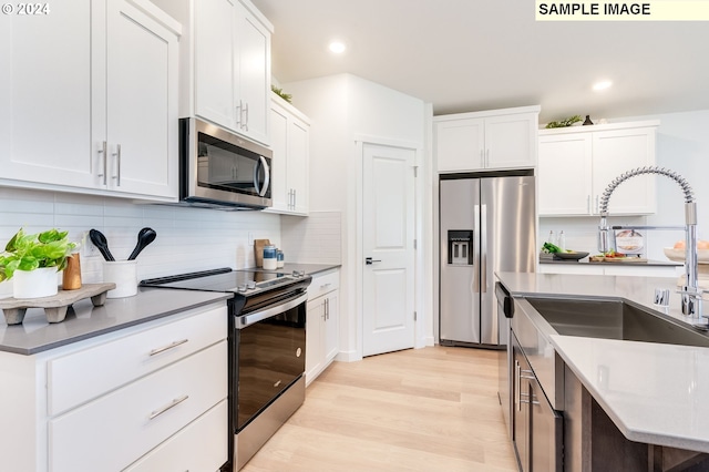 kitchen with light wood finished floors, a sink, stainless steel appliances, white cabinetry, and backsplash