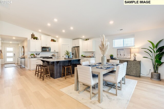 dining space with light hardwood / wood-style flooring, vaulted ceiling, and sink