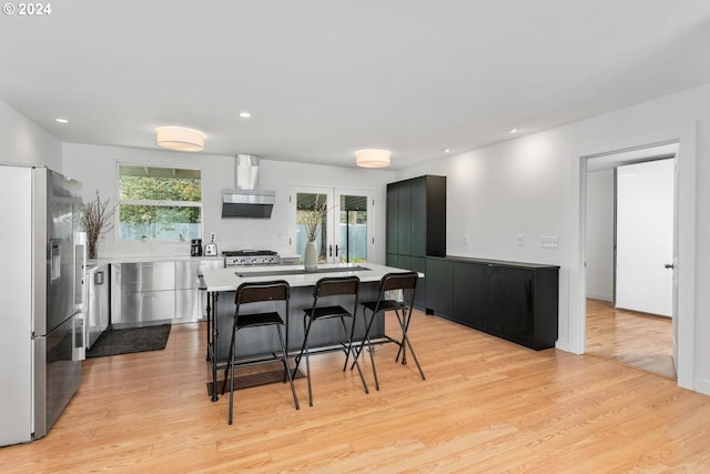 kitchen with wall chimney range hood, a breakfast bar area, light hardwood / wood-style flooring, a kitchen island, and stainless steel appliances