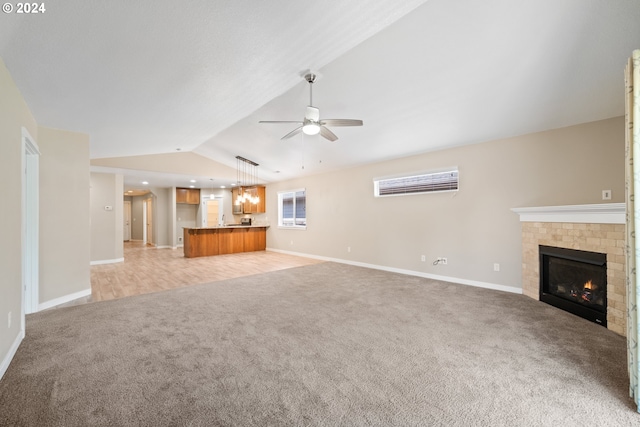 unfurnished living room with ceiling fan, lofted ceiling, light carpet, and a tiled fireplace