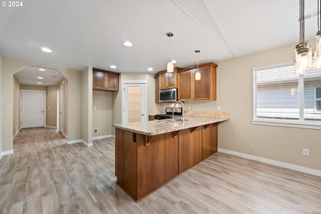 kitchen with light stone counters, hanging light fixtures, stainless steel appliances, and light hardwood / wood-style floors